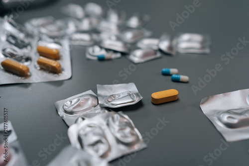 Fotografie Pills, capsules, and numerous empty blister packs lying on dark gray surface, illustrating themes of drug consumption, illness management, health support, and pharmaceutical product usage