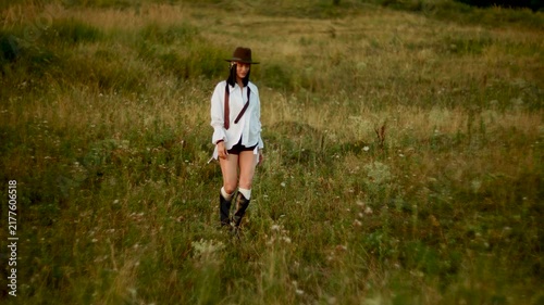 Woman in a brown hat walking through the tall green grass during a warm summer evening sunset