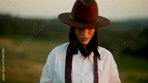 Woman wearing a brown fedora hat standing in a meadow during the golden sunset hour