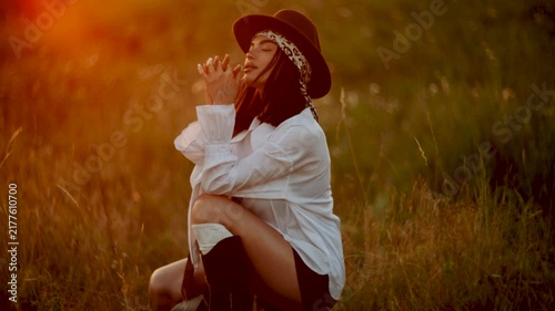 Woman posing in white shirt and hat at sunset in a quiet field during the golden hour