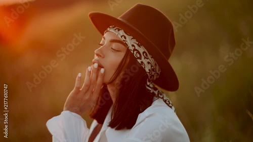 Young woman wearing a brown hat and white shirt poses during a golden sunset in a field