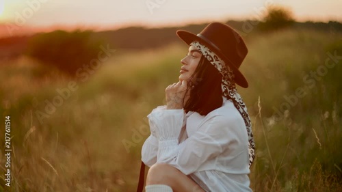 Young woman wearing a hat and white shirt posing in a sunny field during golden hour sunset