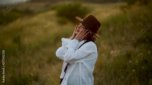 Young woman wearing a hat posing in a grassy field during the golden sunset light