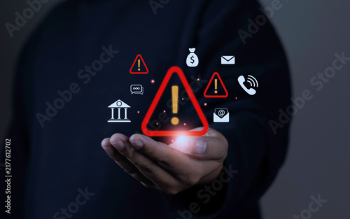 Bank fraud warning and financial scam detection concept with hand holding red warning alert icon surrounded by banking, money, email phishing, and phone risk icons on dark background.