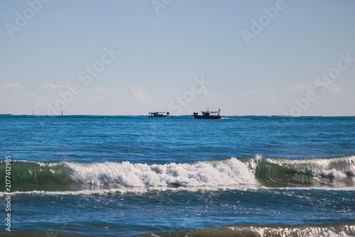 Fotografía Fishing boats on horizon beyond breaking sea waves