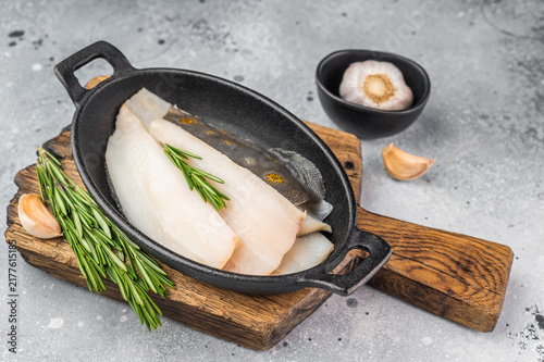 Foto Raw fluke flatfish fillet pieces with rosemary and garlic in iron pan on wooden