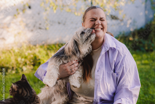 Happy Woman Laughing As Her Small Dog Licks Her Face In A Sunny Backyard Moment