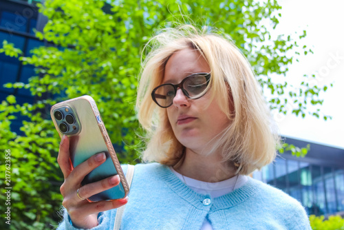 Warsaw, Poland, May 15, 2026. Medium portrait of blonde woman looking intently at smartphone screen outdoors. High quality photograph