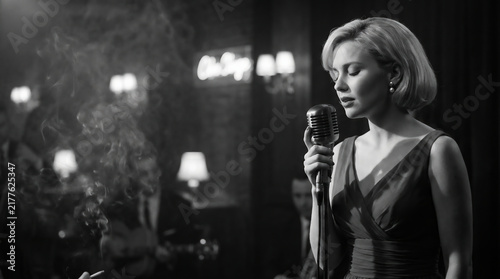 Elegant female jazz singer performing with a vintage microphone in a dimly lit nightclub, captured in timeless black and white cinematic style.