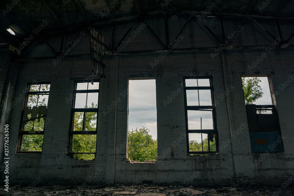 Fototapeta premium Interior of abandoned airplane hangar with broken windows framing lush greenery outside, contrasting decay with nature