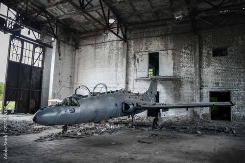 Old jet trainer aircraft abandoned in industrial hangar, wings and body showing heavy decay over time
