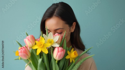 Woman smelling bouquet of tulips and daffodils then looking at camera. Spring, celebration, gift giving, floral arrangement, happiness.