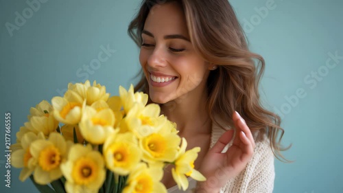 Woman smiling while holding and smelling a bouquet of yellow daffodils. Spring, celebration, happiness, floral arrangement, gift giving.