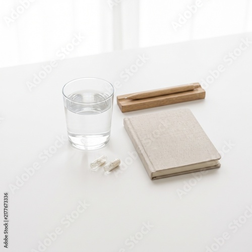 Morning wellness routine items with glass of water, notebook, and wooden pen on white table