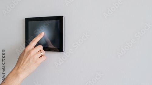 Hand touching smart home control panel on wall for automation and digital house management.