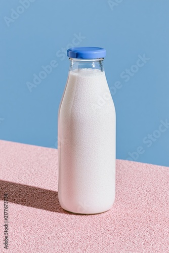 Minimal glass bottle of fresh milk on a pastel pink surface against a blue background, clean modern food concept