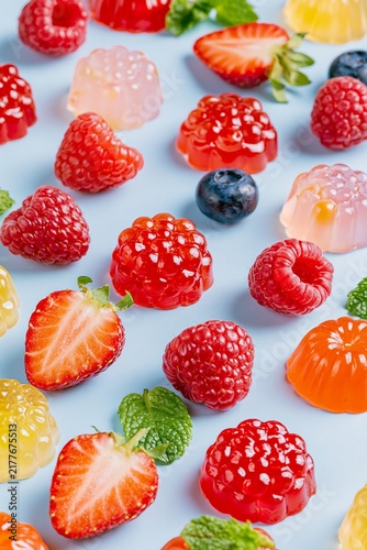 Playful assortment of colorful fruit jelly candies mixed with fresh berries and mint on a pastel blue surface