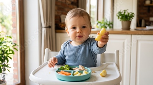 Adorable baby learning independent feeding, enjoying a nutritious meal of vegetables, chicken, and fruit in a high chair. This promotes healthy child development and modern parenting.