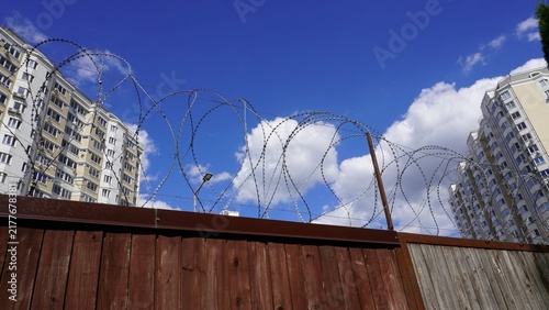 Bild auf Leinwand Wooden fence with barbed wire and apartments