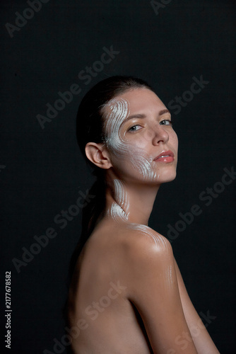 Fotografie A portrait of a nude young woman with white artistic makeup on her face and neck