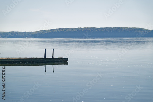 Фотография Calm lake with wooden dock and metal ladder reflecting on still water under clea
