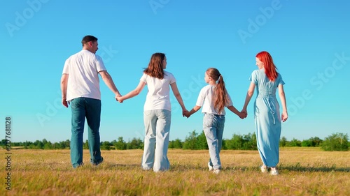 Dad Mom, children daughters walk outdoors. Parents dad mom, daughter playing together on grass holding hands. Happy family go through green meadow, nature blue sky. Family picnic children. Slow motion