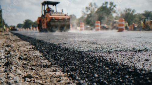 Cuadro en lienzo A close-up view of fresh asphalt being laid on a road construction site with a steamroller compacting the material in the background