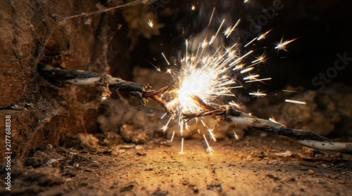 Фотография A close-up shot of a damaged electrical cable sparking on a dusty wooden floor, highlighting a dangerous household electrical hazard