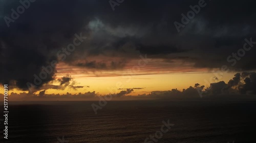 Heavy storm clouds hang above the Atlantic Ocean while warm sunlight illuminates the horizon before sunset.