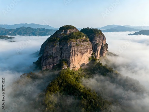 Aerial view of a majestic rock formation rising above a sea of clouds in a mountainous landscape