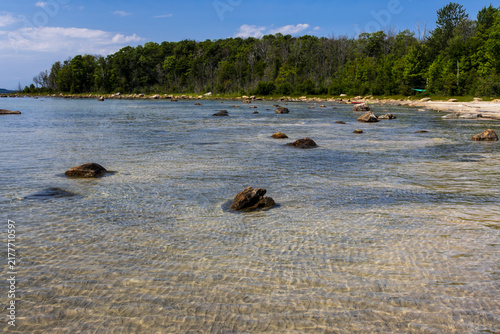 Obraz na płótnie Calm lake shoreline with clear water, sandy beach, and large glacial erratic rocks