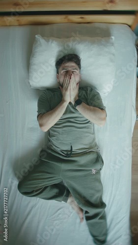 Man waking up peacefully in bed with content smile, top view stretching ,vertical video