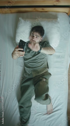Man overwhelmed by phone scrolling in bed, tired eyes and social media fatigue ,vertical video