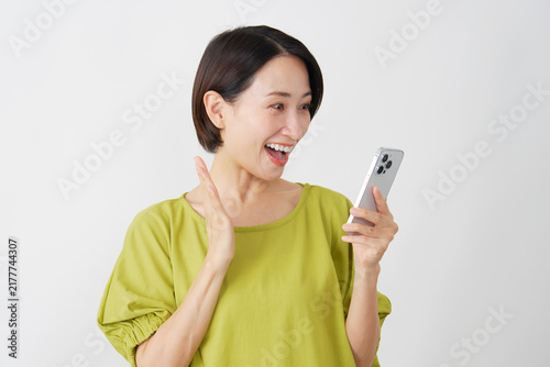 スマホを持って笑顔で驚くミドル女性　白背景