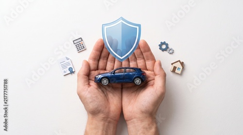 Hands of a person protecting a miniature car with a shield icon, representing car insurance and safety.