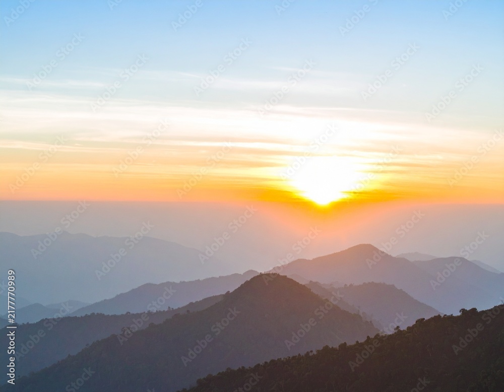 Obraz premium Beautiful sunrise over layered mountain silhouettes in the morning.