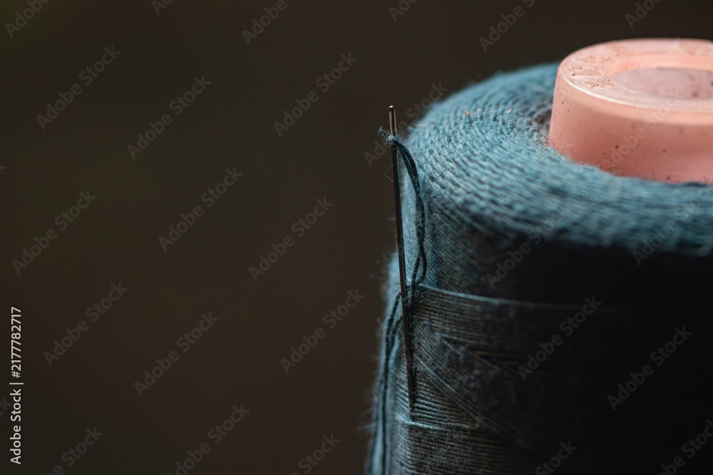 Obraz premium Macro close-up of a steel sewing needle with threaded fiber inserted in a teal thread spool