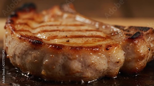 Macro slow motion of a sizzling thick pork chop being grilled, showing beautiful sear marks and juicy caramelized crust cooking in hot fat.
