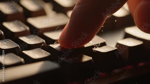 A close-up shot of a finger pressing a dusty key on a backlit computer keyboard.