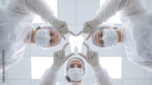 Patient POV Looking Up At Two Dentists In Protective Gear Forming Tooth Shape With Hands White Concept