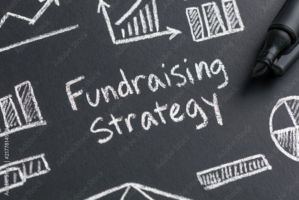 Fototapeta premium Fundraising strategy written on a chalkboard with business finance charts graphs marketing planning and charity