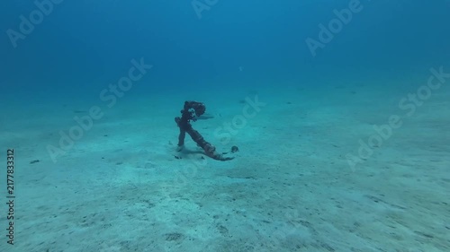Rusty old anchor lies abandoned on a sandy ocean floor. Underwater footage capturing the weathered texture of the historical artifact in deep blue water.