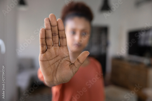 Close up of young Ethiopian woman standing indoors with her hand extended toward camera in stop gesture, powerful sign symbolizes refusal, rejection, personal boundaries, self-defense, self-respect
