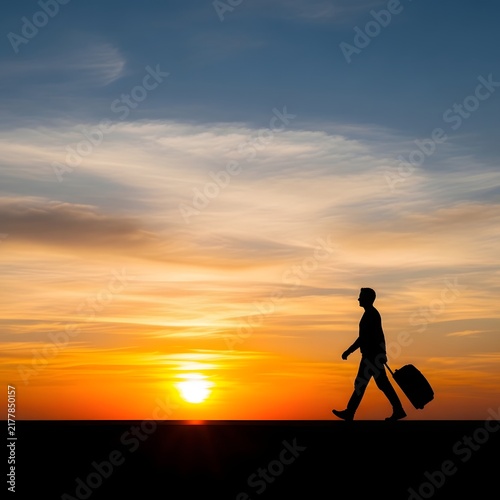 Silhouette of person walking with suitcase at sunset