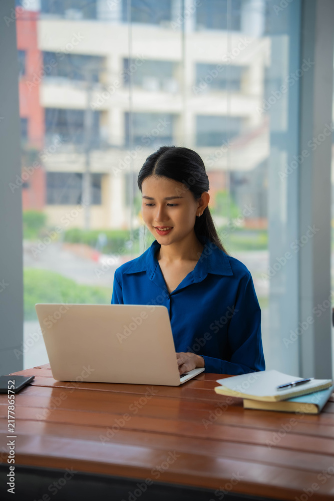 Obraz premium Asian businesswoman in blue shirt typing on laptop
