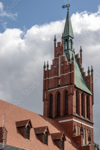 Obraz na płótnie Red brick church tower with a tall green spire rising above a tiled rooftop agai