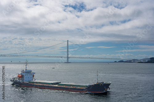 Unmarked cargo ship sails by suspension bridge in Awaji Straight on sunny day