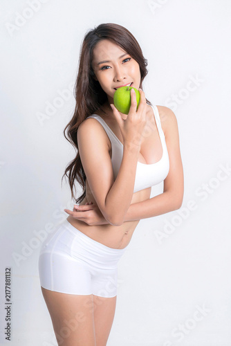 фотографія Fit and attractive asian woman dressed in white sportswear confidently hold a green apple representing balanced diet and commitment to health studio shot on white background