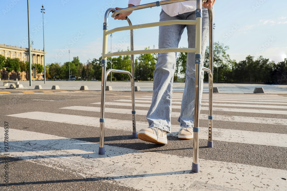 Obraz premium Healthy aging and mobility support, person using a walker to cross a city street for independent living and accessibility in an urban environment