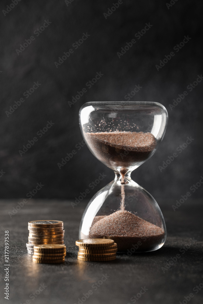 Obraz premium Time is money concept hourglass with falling sand and stacks of coins financial planning investment growth and economic deadline pressure